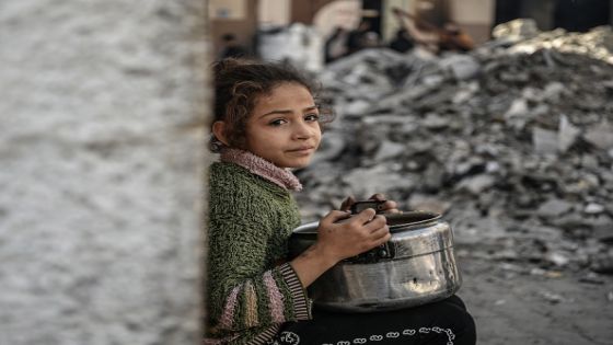 RAFAH, GAZA - DECEMBER 22: A Palestinian child, holding empty pot, waits near rubbles to receive food distributed by volunteers for Palestinian families ,displaced to Southern Gaza due to Israeli attacks, in Rafah, Gaza on December 22, 2023. In the Gaza, where Israeli attacks persist, thousands of Palestinians are grappling with food shortages. The city of Rafah, which has become a refuge for tens of thousands displaced due to the Israeli attacks, is facing increasing challenges in sourcing food. (Photo by Abed Zagout/Anadolu via Getty Images)