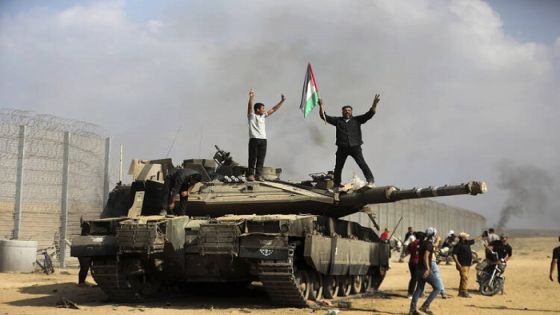 Palestinians wave their national flag and celebrate by a destroyed Israeli tank at the Gaza Strip fence east of Khan Younis southern Saturday, Oct. 7, 2023. The militant Hamas rulers of the Gaza Strip carried out an unprecedented, multi-front attack on Israel at daybreak Saturday, firing thousands of rockets as dozens of Hamas fighters infiltrated the heavily fortified border in several locations by air, land, and sea and catching the country off-guard on a major holiday. (AP Photo/Yousef Masoud)