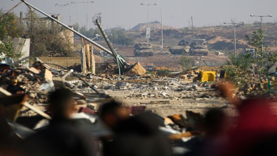 Israeli army Merkava battle tanks and infantry-fighting vehicles (IFVs) take position as displaced Gazans cross the Netzarim corridor from the southern Gaza Strip into Gaza City on January 27, 2025. An unending stream of people marched up the coast of Gaza on January 27, carrying their belongings in plastic bags and repurposed flour sacks through the central city of Nuseirat after Israel reopened access to the territory's north. (Photo by Eyad BABA / AFP) (Photo by EYAD BABA/AFP via Getty Images)