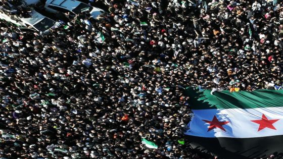 An aerial photo shows crowds of Syrians raising a giant independence-era flag, used by the opposition since the uprising began in 2011, as they celebrate the fall of Bashar al-Assad's iron-fisted rule earlier this week at the central Umayyad Square in Damascus on December 13, 2024. Thousands of jubilant Syrians also gathered outside a landmark mosque in the capital Damascus to celebrate during the first Friday prayers since Assad's ouster on December 8. (Photo by Omar HAJ KADOUR / AFP)