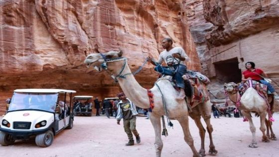 Tourists ride camels and others an electric cart, during their trip to Jordan's famed ancient city of Petra, some 230km (143 miles) south of the capital Amman, on October 27, 2021. - Ten electric carts have replaced 12 of the more traditional animal-powered carriages that transported tourists to the landmark site, in an effort by the authorities to address criticism over animal abuse, among other things. (Photo by Khalil MAZRAAWI / AFP)