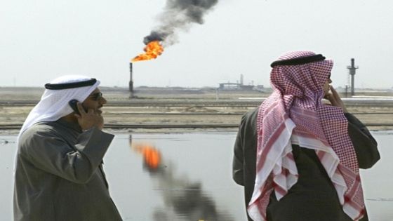 TOPSHOT - Kuwaiti government officials use their cellphone and have a smoke as excess gas is burnt off to the rear at the Kuwait Oil Company (KOC) in al-Ahmadi as it carries oil thru the supply pipeline 05 March 2003. Kuwait supplies 10% of the world's oil and has long since rebuilt it's pipeline systems in a state of the art fashion. AFP PHOTO/Paul J. RICHARDS (Photo by PAUL J. RICHARDS / AFP) (Photo by PAUL J. RICHARDS/AFP via Getty Images)