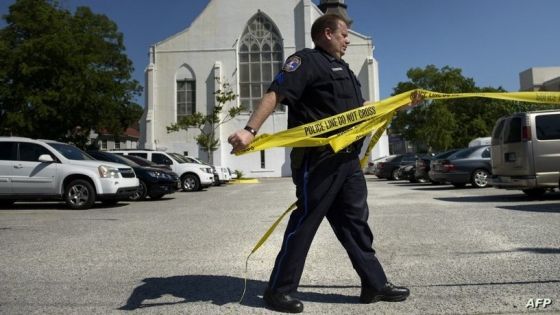 A police officer pulls police tape back to allow cars to enter after Emanuel AME Church was reopened on June 20, 2015 in Charleston, South Carolina. A website apparently created by Dylann Roof emerged Saturday in which the accused Charleston church shooter rails against African Americans and appears in photographs with guns and burning the US flag. His arrest warrant revealed how on June 17 he allegedly shot the six women and three men, aged 26 through 87, multiple times with a high-caliber handgun and then stood over a survivor to make a "racially inflammatory" statement. AFP PHOTO/BRENDAN SMIALOWSKI (Photo by BRENDAN SMIALOWSKI / AFP)