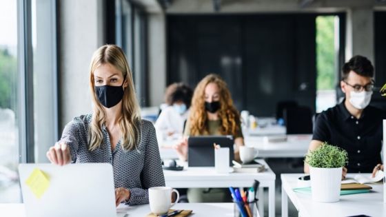 Young people with face masks back at work in office after coronavirus quarantine and lockdown.