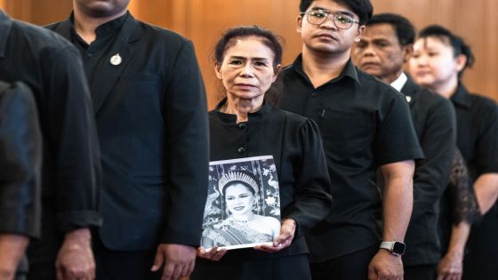 A mourner holds a portrait of Thailand's former Queen Sirikit while lining up to pay respects to the late queen at the Grand Palace in Bangkok on October 26, 2025. The year-long funeral ceremony of Thailand's former Queen Sirikit started on October 26, with grieving royalists set to salute the procession bringing her remains to lie in state at Bangkok's Grand Palace. (Photo by Chanakarn Laosarakham / AFP)