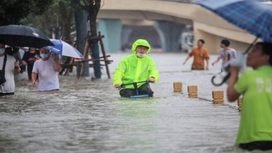 This photo taken on July 20, 2021 shows a man riding a bicycle through flood waters along a street following heavy rains in Zhengzhou in China's central Henan province. (Photo by STR / AFP) / China OUT