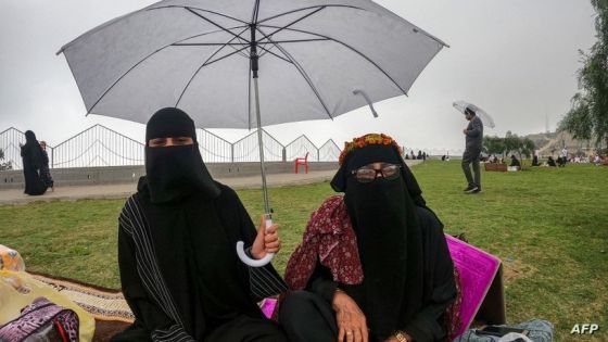 A woman holds an umbrella while she sits with another along a promontory in al-Namas in Saudi Arabia's Asir province, on August 16, 2022. - As Saudi Arabia swelters in temperatures up to 50 degrees Celsius, some are escaping to the "City of Fog" -- a mountainous oasis of cool where warm clothing is needed even in summer. (Photo by Rania SANJAR / AFP)