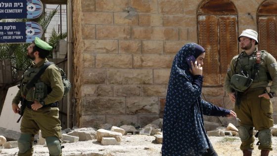 A Palestinian girl talks on her mobile phone passes by Israeli soldiers during a visit by former Israeli soldier Elor Azaria to friends in the settlement of Tal Rumeida in the occupied West Bank city of Hebron on July 3, 2018. - Azaria, a former Israeli soldier who was convicted of manslaughter and sentenced to 18 months imprisonment for killing a wounded and incapacitated Palestinian assailant, was initially condemned to 18 months in prison for the 2016 killing of Abdul Fatah al-Sharif in the occupied West Bank city of Hebron. His term was later reduced the term by four months and in March 2018 a parole board ordered a further cut, with him being released on May 8. (Photo by HAZEM BADER / AFP) (Photo credit should read HAZEM BADER/AFP via Getty Images)