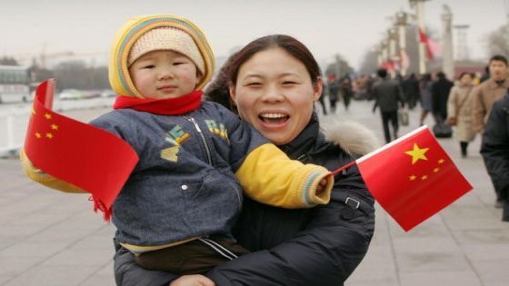 BEIJING, CHINA: A mother carries her child waving Chinese flags near Tiananmen Square in Beijing, 28 February 2005. Chinese lawmakers are suggesting making it a criminal act to conduct ultrasound tests on unborn babies merely to determine their sex aimed at stemming a wave of abortions of female foetuses as families seek boys as their only child. AFP PHOTO/Peter PARKS (Photo credit should read PETER PARKS/AFP/Getty Images)