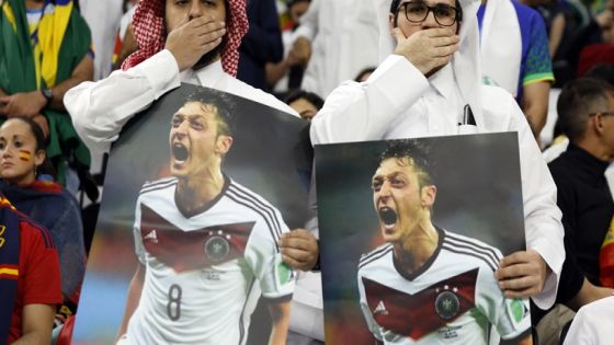 Soccer Football - FIFA World Cup Qatar 2022 - Group E - Spain v Germany - Al Bayt Stadium, Al Khor, Qatar - November 27, 2022 Fans cover their mouths while holding pictures of former Germany player Mesut Ozil REUTERS/John Sibley