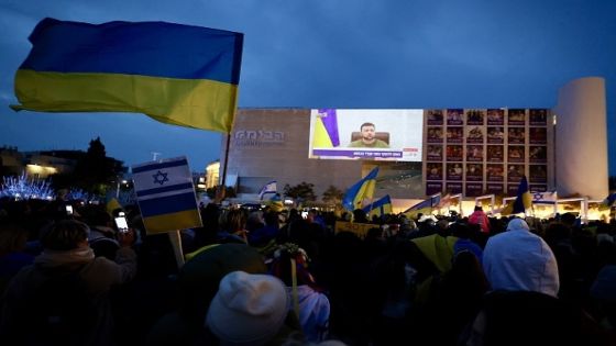 TEL AVIV, ISRAEL - MARCH 20: People, holding banners and flags, are seen during Ukrainian President Volodymyr Zelenskyâs speech on Knesset ( Israelâs parliament) via video conference, in Tel Aviv, Israel on March 20, 2022. A giant screen is set up at Habima Square. (Photo by Mostafa Alkharouf/Anadolu Agency via Getty Images)