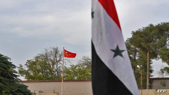 This picture taken on October 18, 2019 from the Syrian Kurdish town of Kobane, also known as Ain al-Arab, along the border with Turkey in the north of Aleppo governorate, shows (foreground) a Syrian government national flag and (background) a Turkish national flag flying across both sides of the border between Syria and Turkey. - Syrian regime troops and Russian soldiers on October 16 entered the key border town of Kobane, following a deal struck with Kurdish authorities amid a deadly Turkish offensive. Kobane is a highly symbolic town for Syria's Kurds, whose forces had in 2015 wrested the town from Islamic State (IS) group control in an epic battle backed by the US-led coalition. (Photo by AFP)