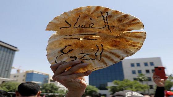 A Jordanian protester holds a loaf of bread with a slogan in arabic reading, "corruption = hunger" during an anti-austerity rally, on June 6, 2018, in front of the Labor Union offices in Amman. - Jordanian unions staged a nationwide strike today over IMF-backed austerity measures including a proposed income tax law that has sparked a week of angry demonstrations. (Photo by AHMAD GHARABLI / AFP) (Photo credit should read AHMAD GHARABLI/AFP/Getty Images)