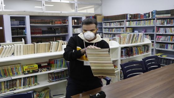 A teacher holds books after he disinfected them as part of sterilization campaign against the new coronavirus, at the library of the Evangelical School, in Loueizeh, east of Beirut, Lebanon, Monday, March 2, 2020. Lebanon's Ministry of Education on Friday, ordered all schools and universities closed for one week over concerns of the virus. (AP Photo/Hussein Malla)