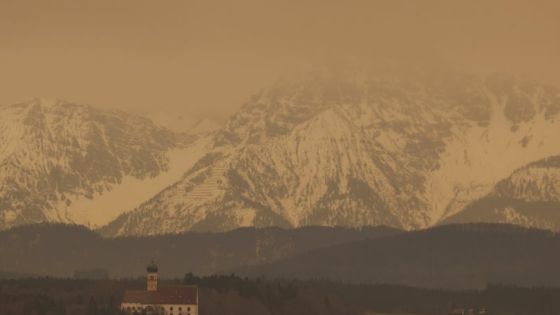 15 March 2022, Bavaria, Ruderatshofen: Dust from the Sahara colors the sky above the Alps and the parish church of St. Martin in Marktoberdorf in reddish hues. The associated clouding of the sky can make the sun appear milky even in otherwise cloud-free skies. Photo: Karl-Josef Hildenbrand/dpa (Photo by Karl-Josef Hildenbrand/picture alliance via Getty Images)