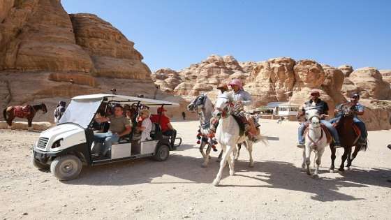 Jordanian men ride horses as tourists ride an electric cart, during their trip to Jordan's famed ancient city of Petra, some 230km (143 miles) south of the capital Amman, on October 27, 2021. - Ten electric carts have replaced 12 of the more traditional animal-powered carriages that transported tourists to the landmark site, in an effort by the authorities to address criticism over animal abuse, among other things. (Photo by Khalil MAZRAAWI / AFP) (Photo by KHALIL MAZRAAWI/AFP via Getty Images)