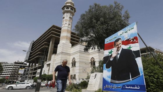 A Syria man walks past a giant portrait of President Bashar al-Assad at Marjeh square in the centre of capital Damascus on May 3, 2021. - A Syrian former minister and a member of the Damascus-tolerated opposition will face Bashar al-Assad in this month's presidential election, the constitutional court said Monday. The Assad-appointed body approved only three out of 51 applications to stand in the May 26 ballot, among them the 55-year-old president himself, (Photo by LOUAI BESHARA / AFP)