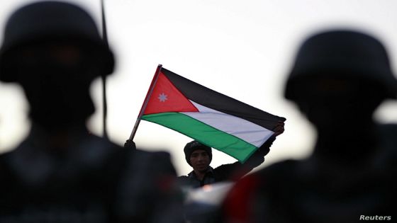 A pro-government supporter holds a Jordanian national flag as he stands near policemen, during a protest by anti-government demonstrators calling themselves the "Youth of March 24 Movement" as they demand political reforms in Amman March 24, 2013. REUTERS/Muhammad Hamed (JORDAN - Tags: POLITICS CIVIL UNREST)