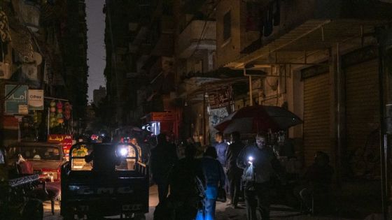 (FILES) A man walks with a flashlight along a darkened street during a power cut in the Fleming neighbourhood of Alexandria on November 25, 2023. Egypt began planned blackouts known as "load shedding" in July 2023 in an attempt to ease the load on local electricity networks as energy consumption surged during the hot summer months. Egypt's economy has struggled in recent years with runaway inflation and repeated depreciations of the local currency, affecting purchasing power and the ability to import key goods. (Photo by Amir MAKAR / AFP)