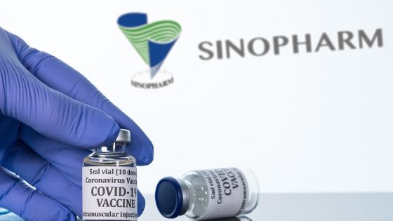 Morgantown, WV - 16 December 2020: Small bottle of coronavirus vaccine with syringe with background of the Chinese company Sinopharm logo