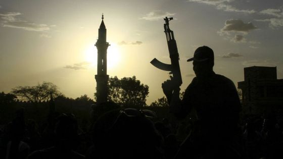 A fighter loyal to Sudan's army chief Abdel Fattah al-Burhan holds up a weapon backdropped by the minaret of a mosque, during a graduation ceremony in the southeastern Gedaref state on May 27, 2024. - Sudan has been in the throes of conflict for over a year between the regular army led by de facto ruler Abdel Fattah al-Burhan and the RSF led by his former deputy Mohamed Hamdan Daglo. (Photo by AFP)