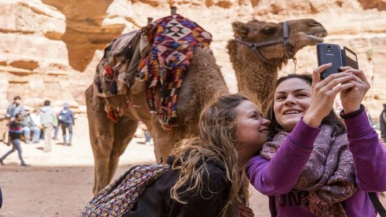 Jordan, Petra, Tourists take selfie snapshots beside camel in front of The Al Khazneh or The Treasury at Petra amid ancient ruins