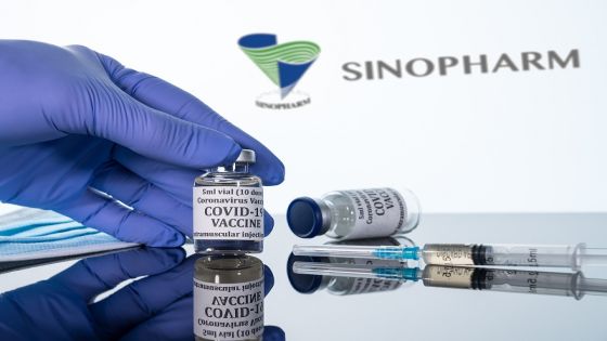 Morgantown, WV - 16 December 2020: Small bottle of coronavirus vaccine with syringe with background of the Chinese company Sinopharm logo
